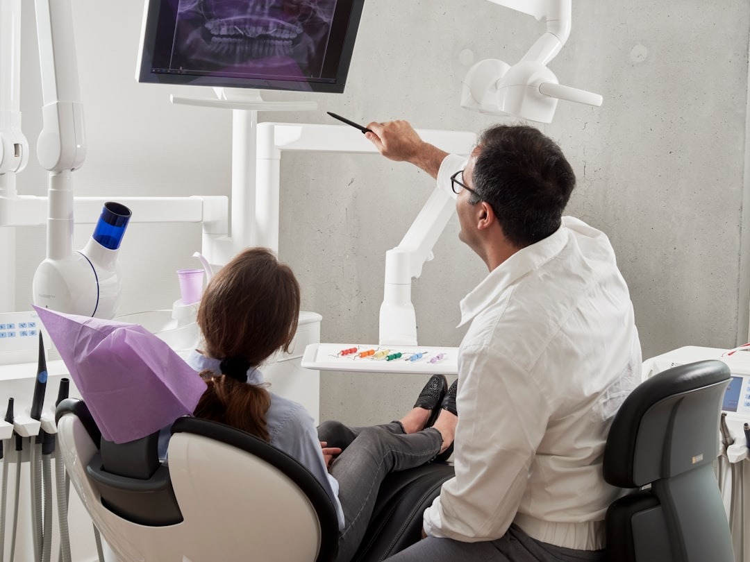 Dentist explains teeth X-ray on monitor to patient in chair.